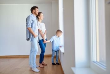 family, people and real estate concept - happy mother, father and little son looking through window at new home or apartment. happy family with child at new home or apartment