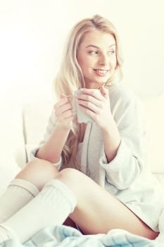morning, leisure and people concept - happy young woman with cup of coffee or tea in bed at home bedroom. happy woman with cup of coffee in bed at home