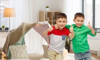 childhood, fashion, friendship and people concept - happy smiling little boys showing thumbs up over kids room and tepee background. happy smiling little boys showing thumbs up