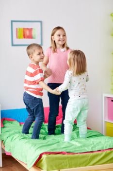 childhood, leisure and family concept - happy little kids jumping on bed at home. happy little kids jumping on bed at home