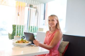 eating, technology, people and leisure concept - happy young woman with tablet pc computer, earphones and food at restaurant. happy young woman with tablet pc at restaurant