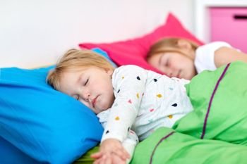 childhood, bedtime and family concept - happy little girls or sisters sleeping in bed at home. happy little girls sleeping in bed at home