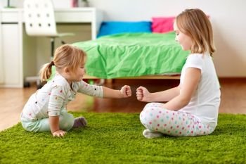 childhood, leisure and family concept - happy little girls playing rock-paper-scissors game or making fist bump at home. girls playing rock-paper-scissors game at home