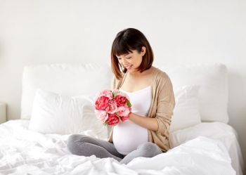 pregnancy, holidays and people concept - happy pregnant asian woman with flowers in bed at home. happy asian pregnant woman with flowers in bed