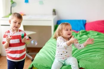 childhood, leisure and people concept - happy kids blowing soap bubbles and playing at home. kids blowing soap bubbles and playing at home