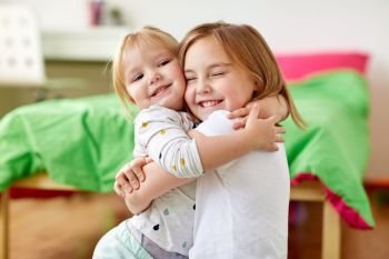childhood, family, expressions and people concept - happy little girls or sisters hugging at home. happy little girls or sisters hugging at home