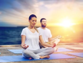 yoga and healthy lifestyle concept - people meditating in lotus pose on wooden pier over sea background. people meditating in yoga lotus pose outdoors