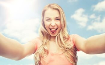 emotions, expressions and people concept - happy smiling young woman taking selfie over blue sky and clouds background. happy smiling young woman taking selfie
