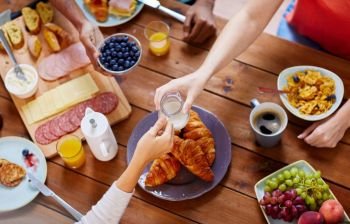 food, eating and family concept - group of people sharing milk or cream for breakfast at wooden table. people having breakfast at table with food
