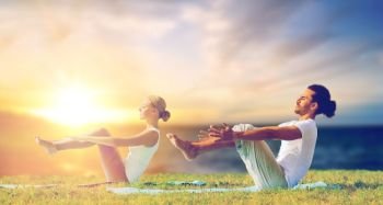 fitness and people concept - couple making yoga half-boat pose outdoors over sea background. couple making yoga half-boat pose outdoors