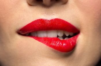 beauty, make up and mouth expression concept - close up of woman face with red lipstick biting lower lip. close up of woman with red lipstick biting lip