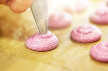 cooking, food and people concept - chef with confectionery bag squeezing macaron batter or meringue cream to baking sheet at pastry shop. chef with nozzle squeezing macaron batter