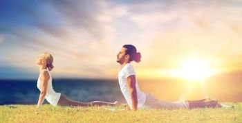 fitness and people concept - couple making yoga cobra pose outdoors over sea background. couple making yoga cobra pose outdoors