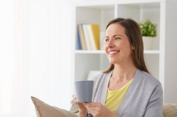 people, drinks and leisure concept - happy middle-aged woman with mug drinking tea or coffee at home. happy woman drinking tea or coffee at home