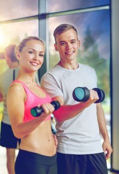 fitness, sport, exercising and diet concept - smiling young woman and personal trainer with dumbbells in gym. smiling young woman with personal trainer in gym