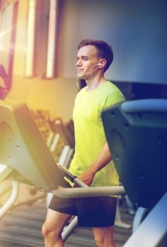 sport, fitness, lifestyle, technology and people concept - man with earphones exercising on treadmill in gym. man with smartphone exercising on treadmill in gym