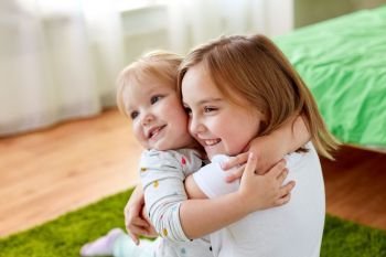 childhood, family, expressions and people concept - happy little girls or sisters hugging at home. happy little girls or sisters hugging at home