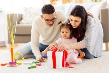 family, holidays and people concept - mother, father and happy little daughter with gift box at home birthday party. baby girl with birthday gift and parents at home . baby girl with birthday gift and parents at home 