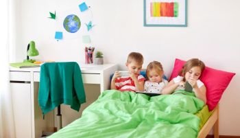 childhood, technology and family concept - little kids with tablet pc computer and smartphones in bed at home. kids with tablet pc and smartphones in bed at home. kids with tablet pc and smartphones in bed at home