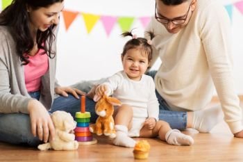 family, holidays and people concept - happy mother, father and little daughter playing with toy rabbit on birthday party. baby girl with parents playing with toy rabbit. baby girl with parents playing with toy rabbit