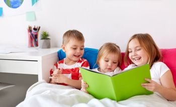 childhood, leisure and family concept - little kids reading book in bed at home. little kids reading book in bed at home. little kids reading book in bed at home