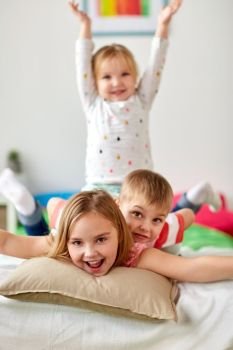 childhood, leisure and family concept - happy little kids having fun in bed at home. happy little kids having fun in bed at home. happy little kids having fun in bed at home