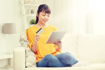 people, internet bank, online shopping, technology and e-money concept - happy asian young woman sitting on sofa with tablet pc computer and credit card at home. happy asian woman with tablet pc and credit card. happy asian woman with tablet pc and credit card