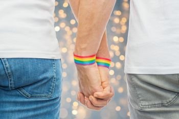lgbt, same-sex relationships and homosexual concept - close up of male couple wearing gay pride rainbow awareness wristbands holding hands over lights background. male couple with gay pride rainbow wristbands. male couple with gay pride rainbow wristbands
