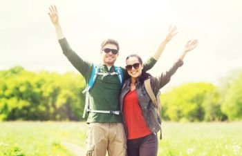 travel, hiking, backpacking, tourism and people concept - happy couple with backpacks waving hands and walking along country road outdoors. happy couple with backpacks hiking outdoors. happy couple with backpacks hiking outdoors