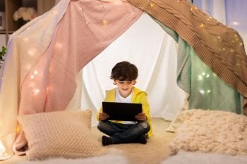 childhood, technology and hygge concept - happy little boy with tablet pc computer in kids tent at home. little boy with tablet pc in kids tent at home. little boy with tablet pc in kids tent at home
