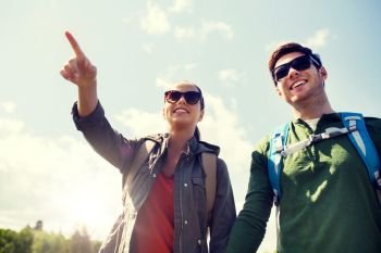 travel, hiking, backpacking, tourism and people concept - happy couple with backpacks walking outdoors and pointing finger to something. happy couple with backpacks hiking outdoors. happy couple with backpacks hiking outdoors
