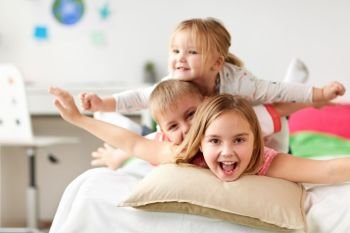 childhood, leisure and family concept - happy little kids having fun in bed at home. happy little kids having fun in bed at home. happy little kids having fun in bed at home
