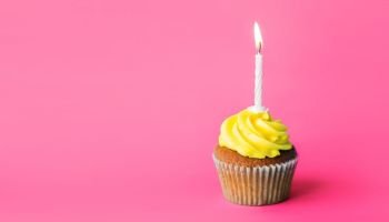holiday, celebration, greeting and party concept - birthday cupcake with one burning candle over pink background. birthday cupcake with one burning candle. birthday cupcake with one burning candle
