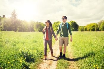 travel, hiking, backpacking, tourism and people concept - happy couple with backpacks holding hands and walking along country road outdoors. happy couple with backpacks hiking outdoors. happy couple with backpacks hiking outdoors