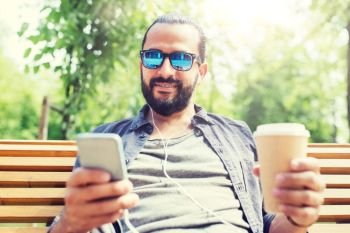 people, music, technology, leisure and lifestyle - man with earphones and smartphone drinking coffee on city street bench. man with earphones and smartphone drinking coffee. man with earphones and smartphone drinking coffee