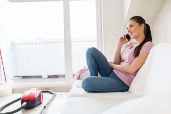 cleaning, household and technology concept - happy woman or housewife calling by smartphone with vacuum cleaner and mop in bucket on floor at home. woman calling by smartphone after cleaning home. woman calling by smartphone after cleaning home