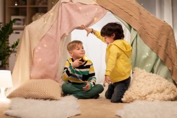 childhood, hygge and friendship concept - happy boys with torch light having fun in kids tent or teepee at home. happy boys with torch light in kids tent at home. happy boys with torch light in kids tent at home