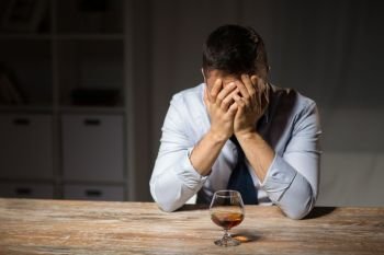 alcoholism, alcohol addiction and people concept - male alcoholic drinking brandy on table at night. drunk man with glass of alcohol on table at night. drunk man with glass of alcohol on table at night