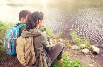 travel, hiking, backpacking, tourism and people concept - couple with backpacks sitting on lake or river bank. couple with backpacks sitting on river bank. couple with backpacks sitting on river bank