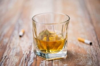alcohol addiction and alcoholism concept - close up of glass of whiskey and cigarette butts on table. glass of alcohol on table and cigarette butts. glass of alcohol on table and cigarette butts