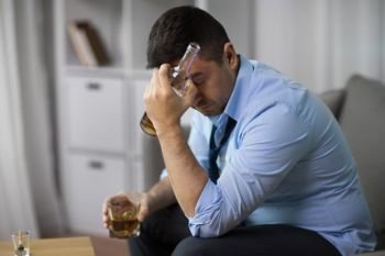 alcoholism, alcohol addiction and people concept - male alcoholic with bottle and glass drinking whiskey at home. alcoholic with bottle drinking whiskey at home. alcoholic with bottle drinking whiskey at home