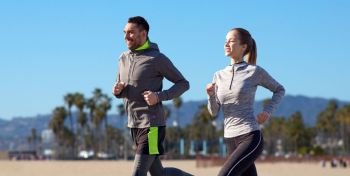 fitness, sport, people and healthy lifestyle concept - happy couple running over venice beach background in california. happy couple running outdoors. happy couple running outdoors