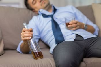 alcoholism, alcohol addiction and people concept - close up of man sleeping with bottle of whiskey on sofa at home. close up of man sleeping with bottle of alcohol. close up of man sleeping with bottle of alcohol