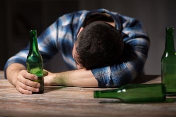 alcoholism, alcohol addiction and people concept - male alcoholic with beer bottles lying or sleeping on table at night. drunk man with beer bottles on table at night. drunk man with beer bottles on table at night