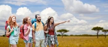 travel, tourism, hike and adventure concept - group of smiling friends with backpacks pointing finger to something over african savannah background. friends with backpacks over african savannah. friends with backpacks over african savannah