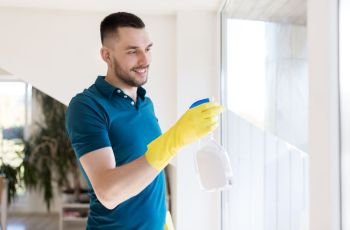 household and people concept - man in rubber gloves cleaning window with spray cleaner at home. man in rubber gloves cleaning window with spray. man in rubber gloves cleaning window with spray