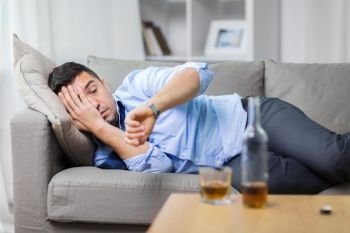 alcoholism, alcohol addiction and people concept - male alcoholic lying on sofa and looking at wristwatch. alcoholic lying on sofa and looking at wristwatch. alcoholic lying on sofa and looking at wristwatch