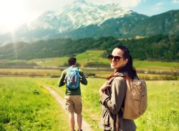 travel, tourism and people concept - happy couple with backpacks walking along country road over mountains background. happy couple with backpacks traveling in highlands. happy couple with backpacks traveling in highlands