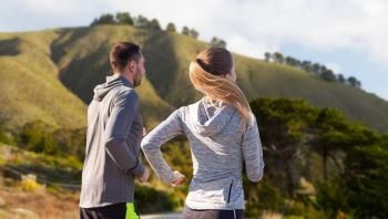 fitness, sport, people and healthy lifestyle concept - happy couple running over big sur hills and road background in california. happy couple running outdoors. happy couple running outdoors