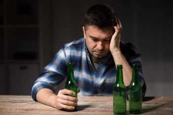 alcoholism, alcohol addiction and people concept - male alcoholic with bottles drinking beer at table at night. drunk man drinking alcohol at table at night. drunk man drinking alcohol at table at night